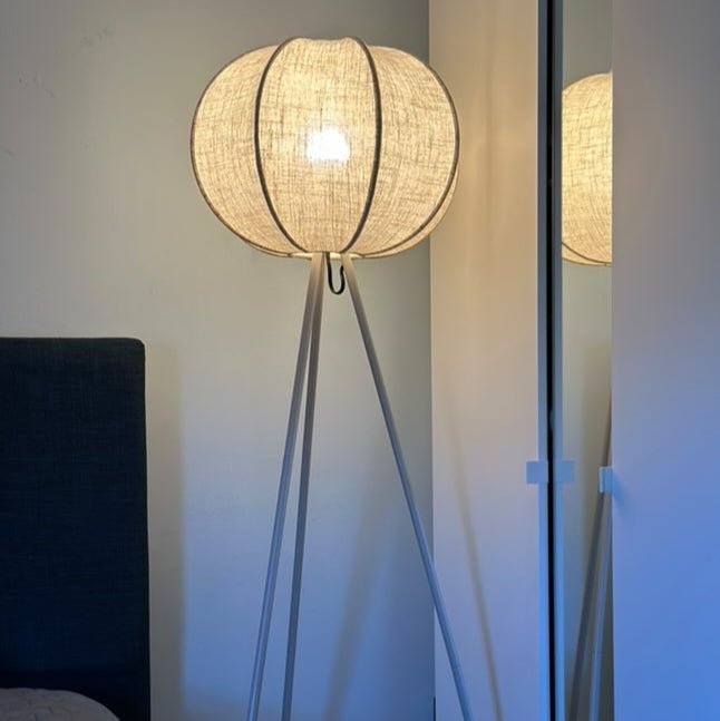 Tripod lamp with linen shade next to armchair